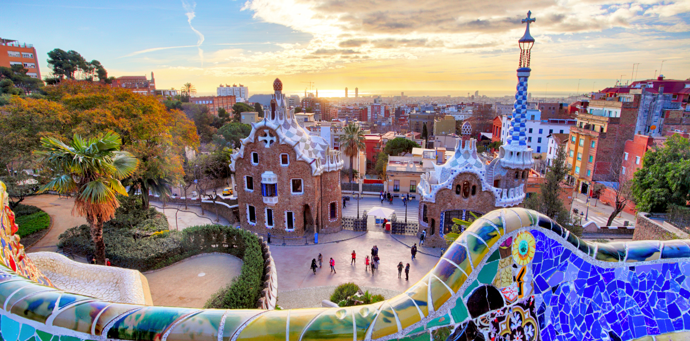 View of Park Güell in Barcelona, Spain, showcasing the park's colorful mosaics and distinctive architectural designs with the cityscape in the background at sunrise—a perfect highlight for those exploring convention destinations.
