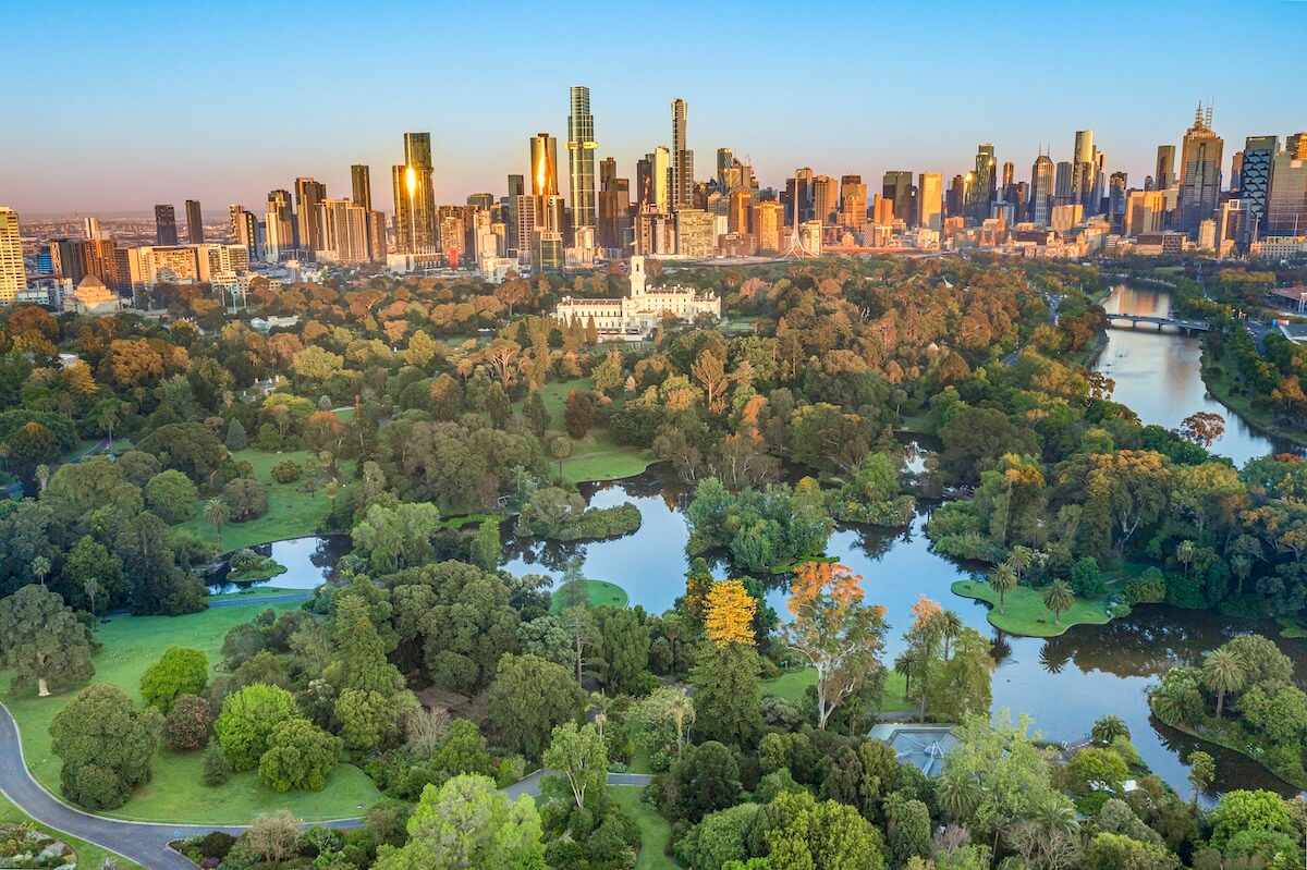 Aerial view of a lush green park with ponds, surrounded by a city skyline at sunset.