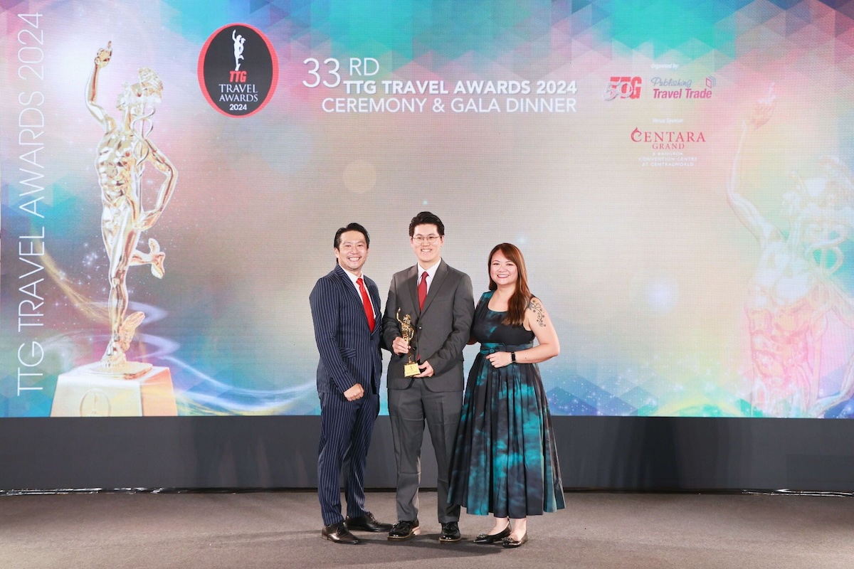 Three people stand in evening attire holding a trophy at the 33rd TTG Travel Awards 2024 ceremony.